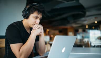 man wearing headphones while sitting on chair in front of MacBook