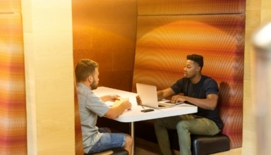 man sitting on black leather bench holding gray laptop computer on top of white wooden table