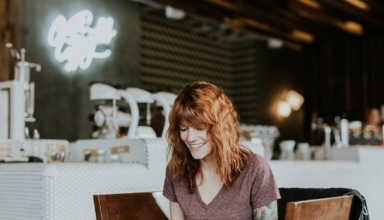 woman sitting on brown wooden chair while using silver laptop computer in room