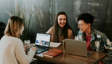 three people sitting in front of table laughing together