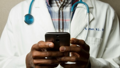 person wearing lavatory gown with green stethoscope on neck using phone while standing