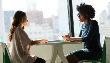 two women sitting beside table and talking